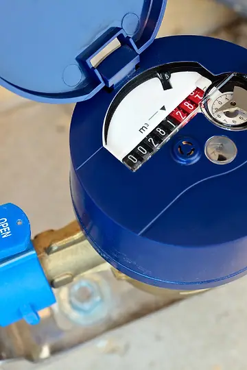 Hidrômetro azul instalado em cano de metal, com a tampa do mostrador aberta