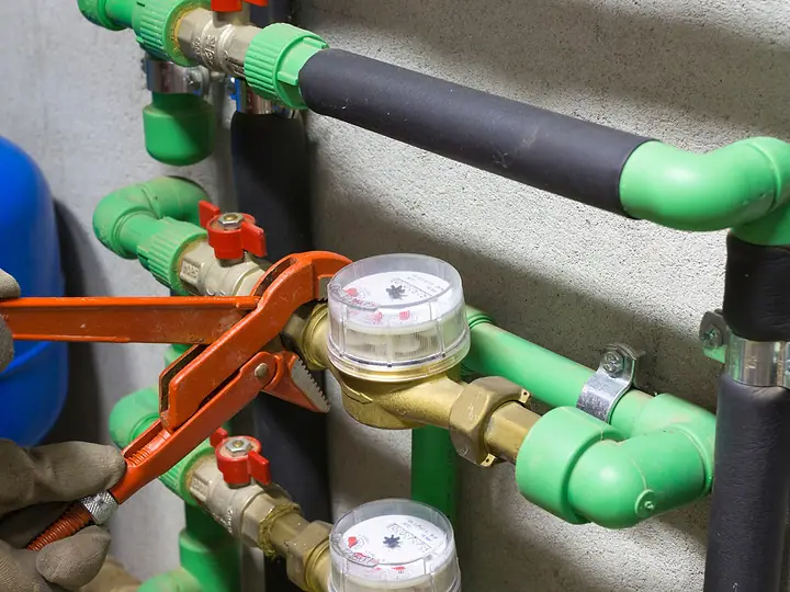Mão apertando com chave de grifo a conexão de um hidrômetro na tubulação verde