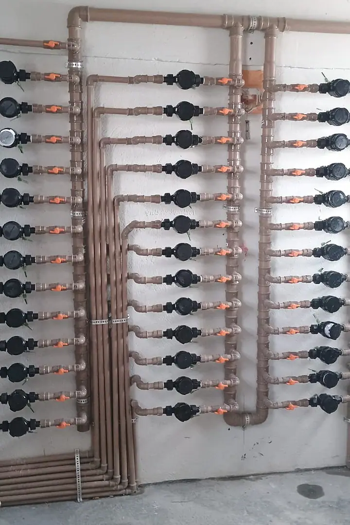 Quadro com hidrômetros individuais instalados em tubulação de cobre na parede de um condomínio