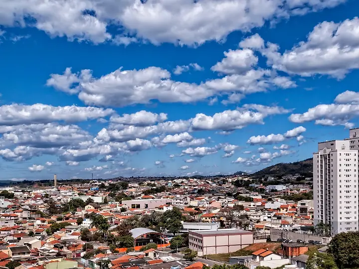 Vista do alto de uma cidade com casas e prédios, sob céu azul com nuvens